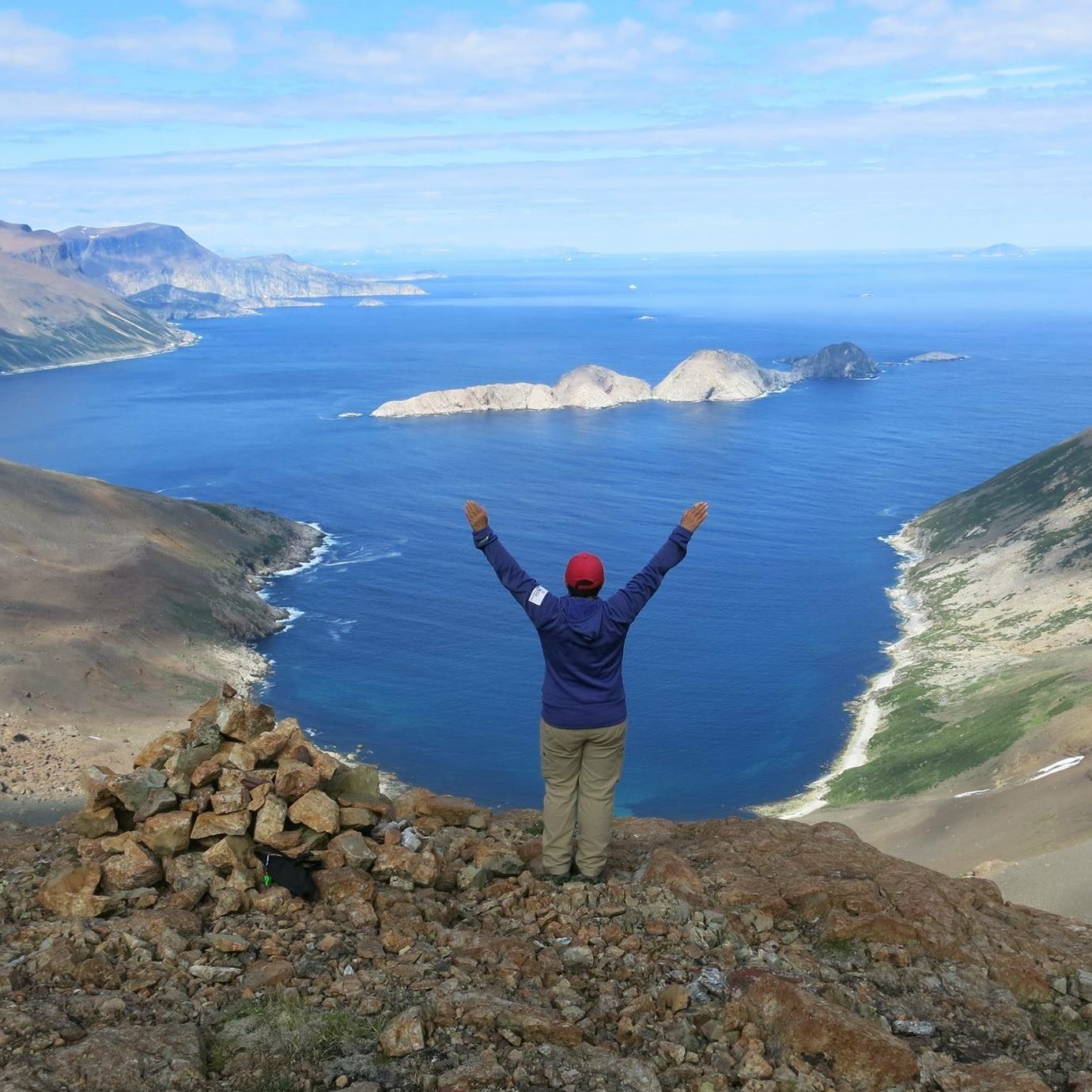 TA standing with arms above head, back on to camera, being amazed at the view of the Labrador Sea